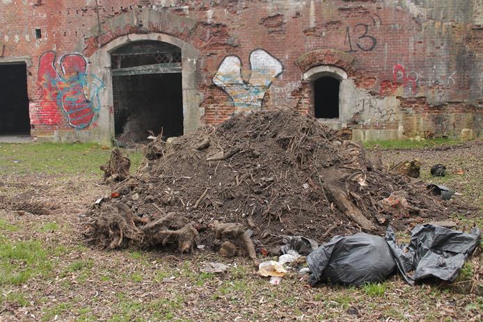 Na tle koszar: kupa Âśmiecia z korzeniami zgarniĂŞta po karczowaniu krzokĂłw z gĂłry, znad koszar.